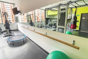 Un gimnasio con equipamiento de ejercicio, un trampolín y un espejo grande que refleja el espacio.