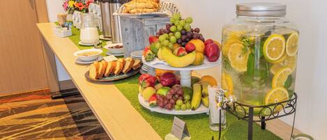 Una mesa de buffet con diversos alimentos y un dispensador grande de ponche de frutas.