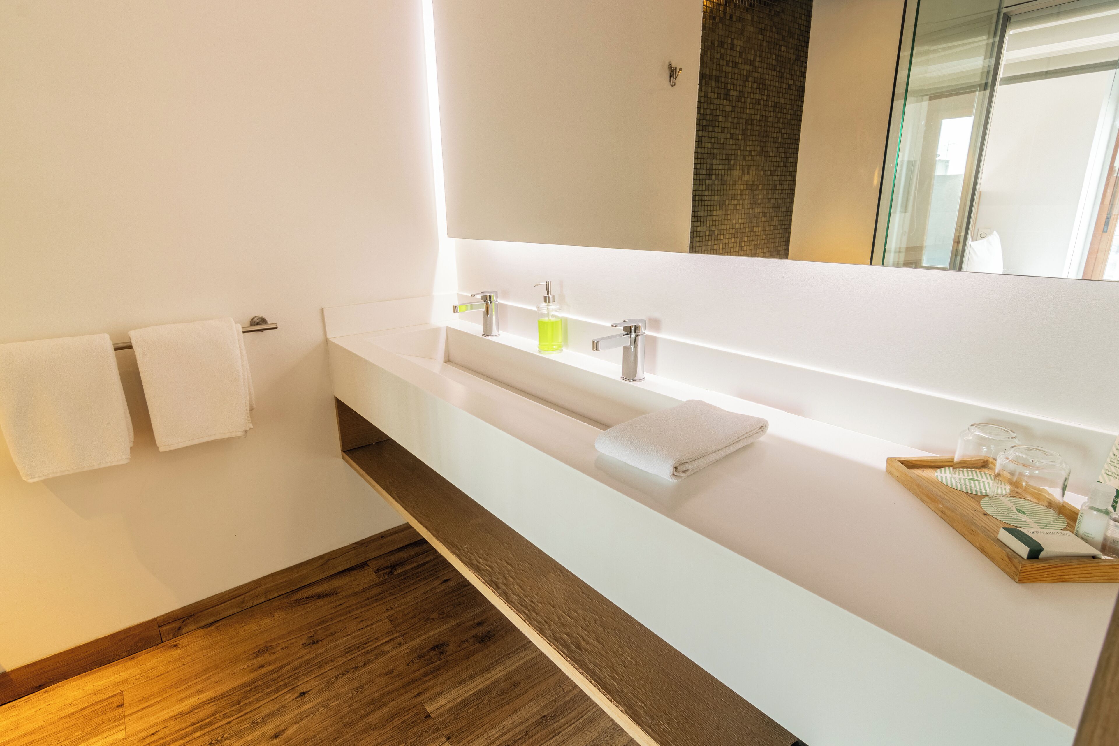 A modern bathroom with a white vanity, two sinks, a large mirror, and a wooden floor.