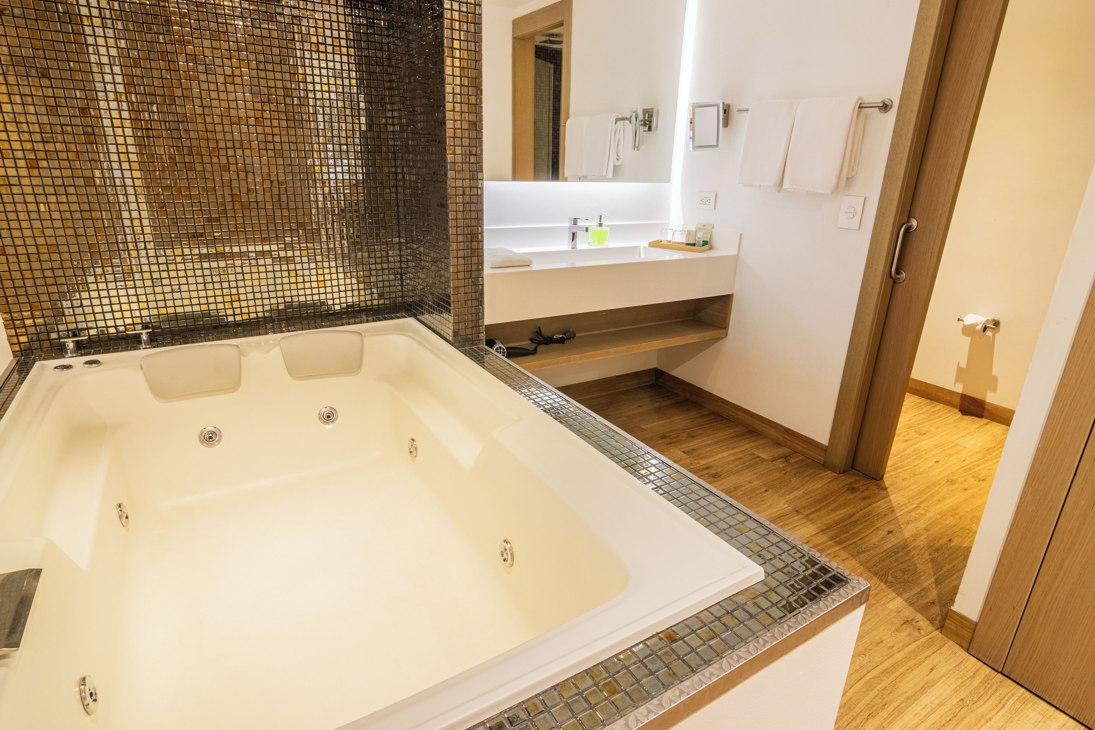 A modern bathroom with a large bathtub, a glass shower enclosure, a wooden floor, and a white vanity with a mirror.