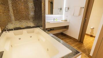 A modern bathroom with a large bathtub, a glass shower enclosure, a wooden floor, and a white vanity with a mirror.