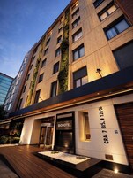 A modern hotel building with a prominent entrance, a name sign, and a contact number.