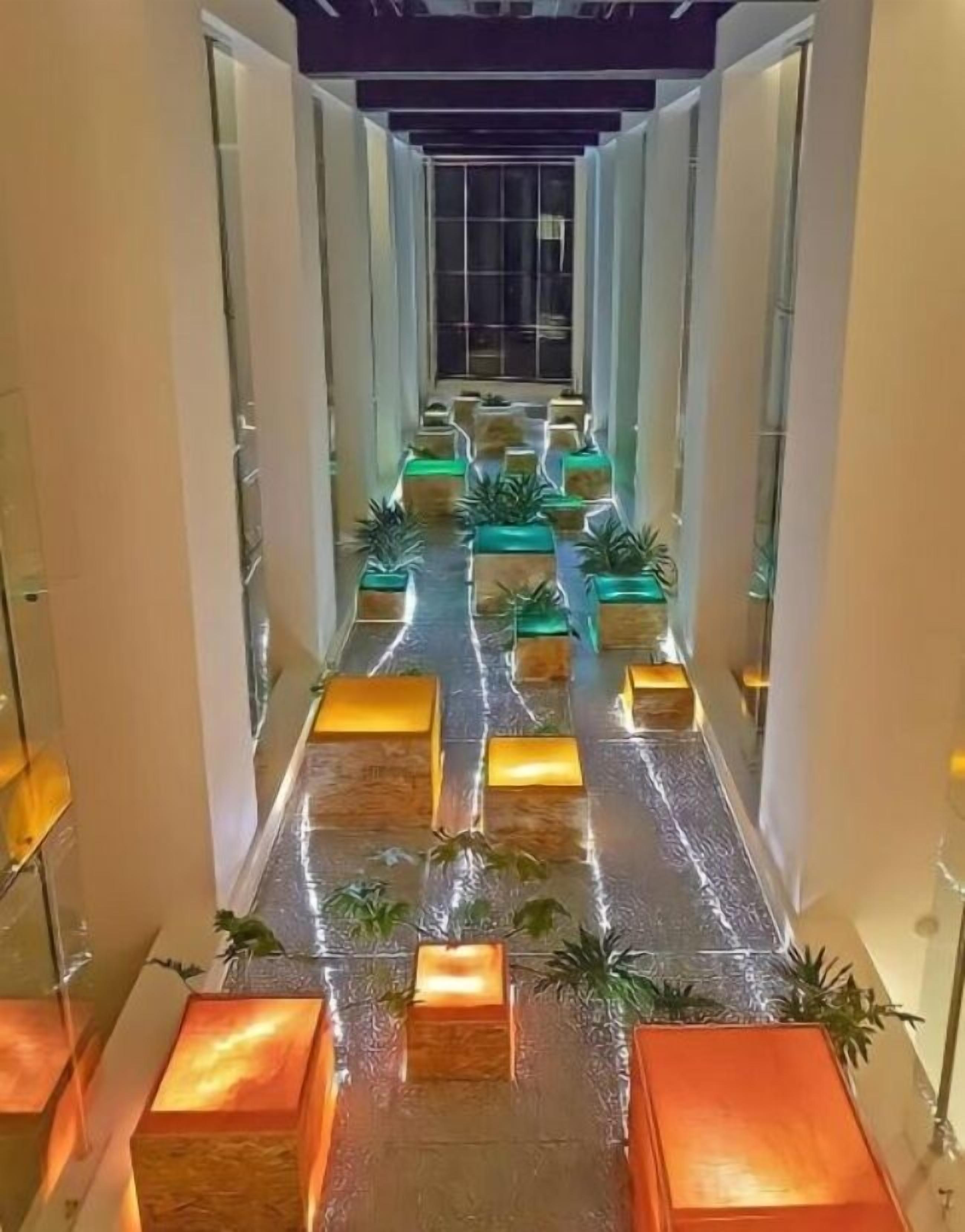 Un pasillo con un camino central, flanqueado por columnas e iluminado con macetas verdes.