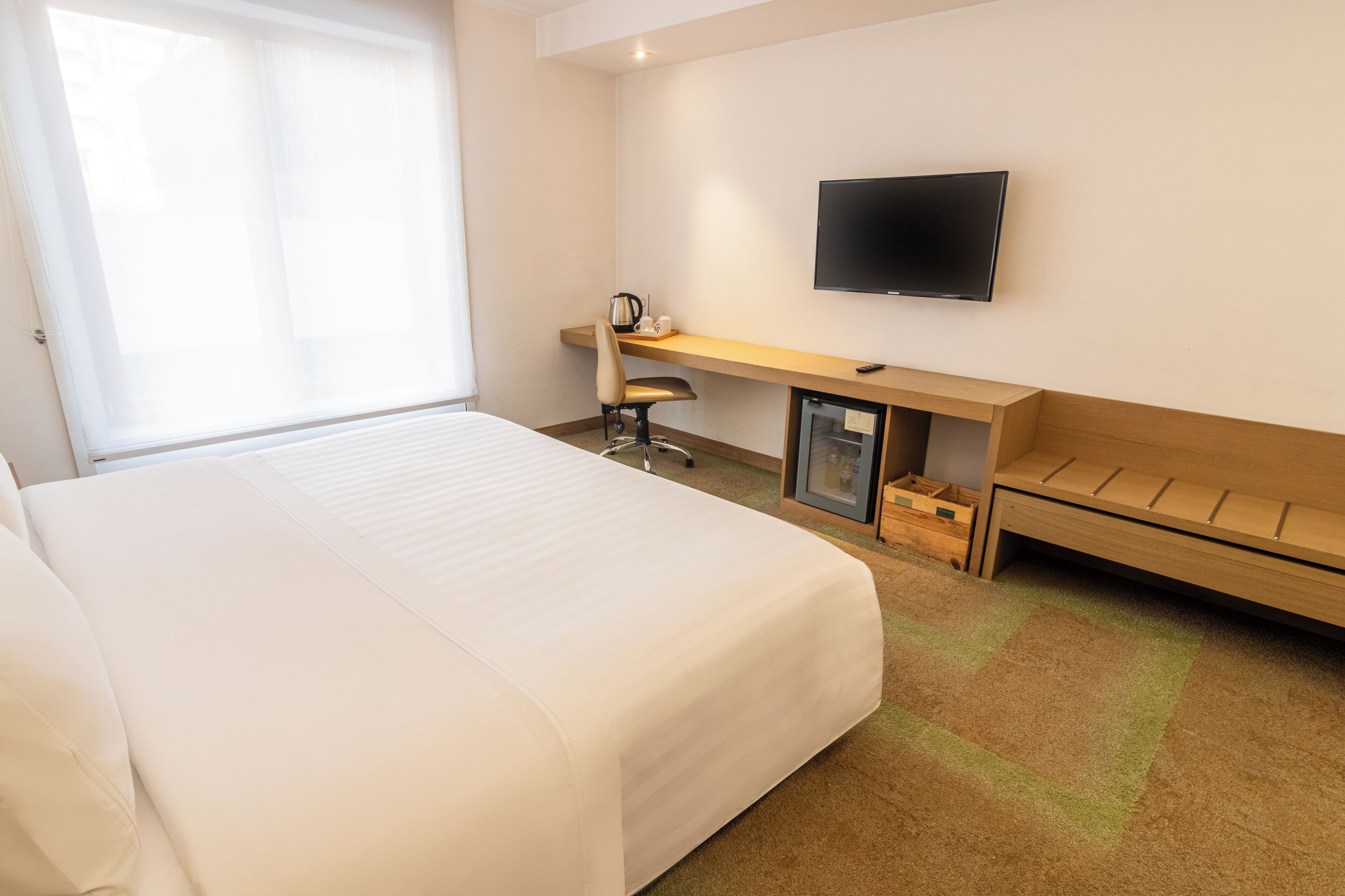 A hotel room with a large bed, a desk with a chair, a television, and a small cabinet.