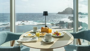 Una mesa de desayuno con vista al océano, una lámpara y una cesta de fruta.