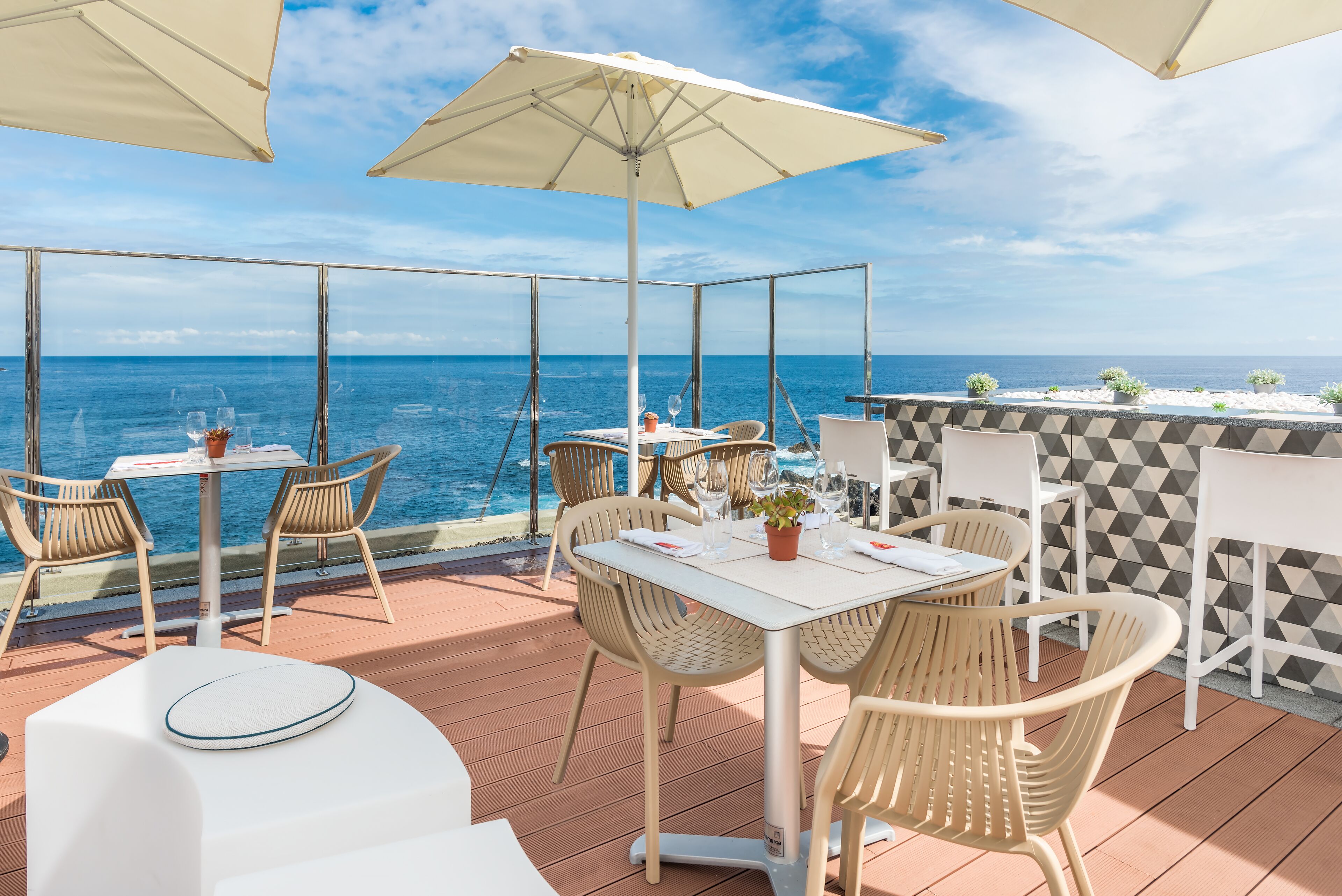 An outdoor dining area with tables and chairs, overlooking the sea.