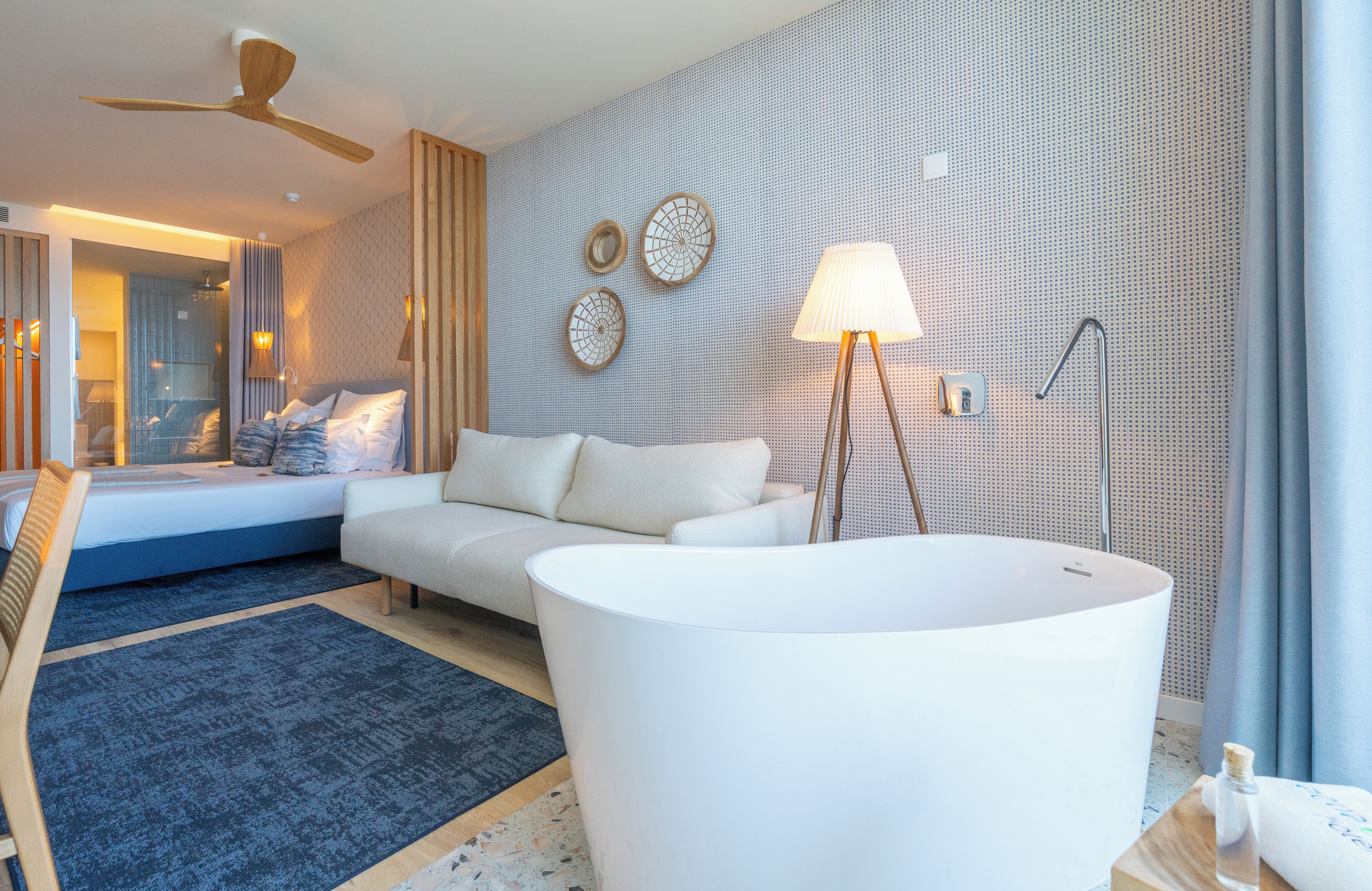 Ett modernt hotellrum med ett stort vitt badkar, en soffa och en takfläkt.