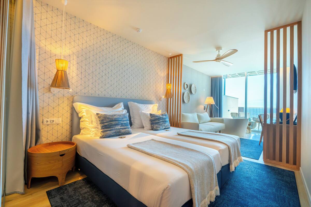 A modern hotel room with a large bed, bedside lamps, a ceiling fan, and a view of the balcony.