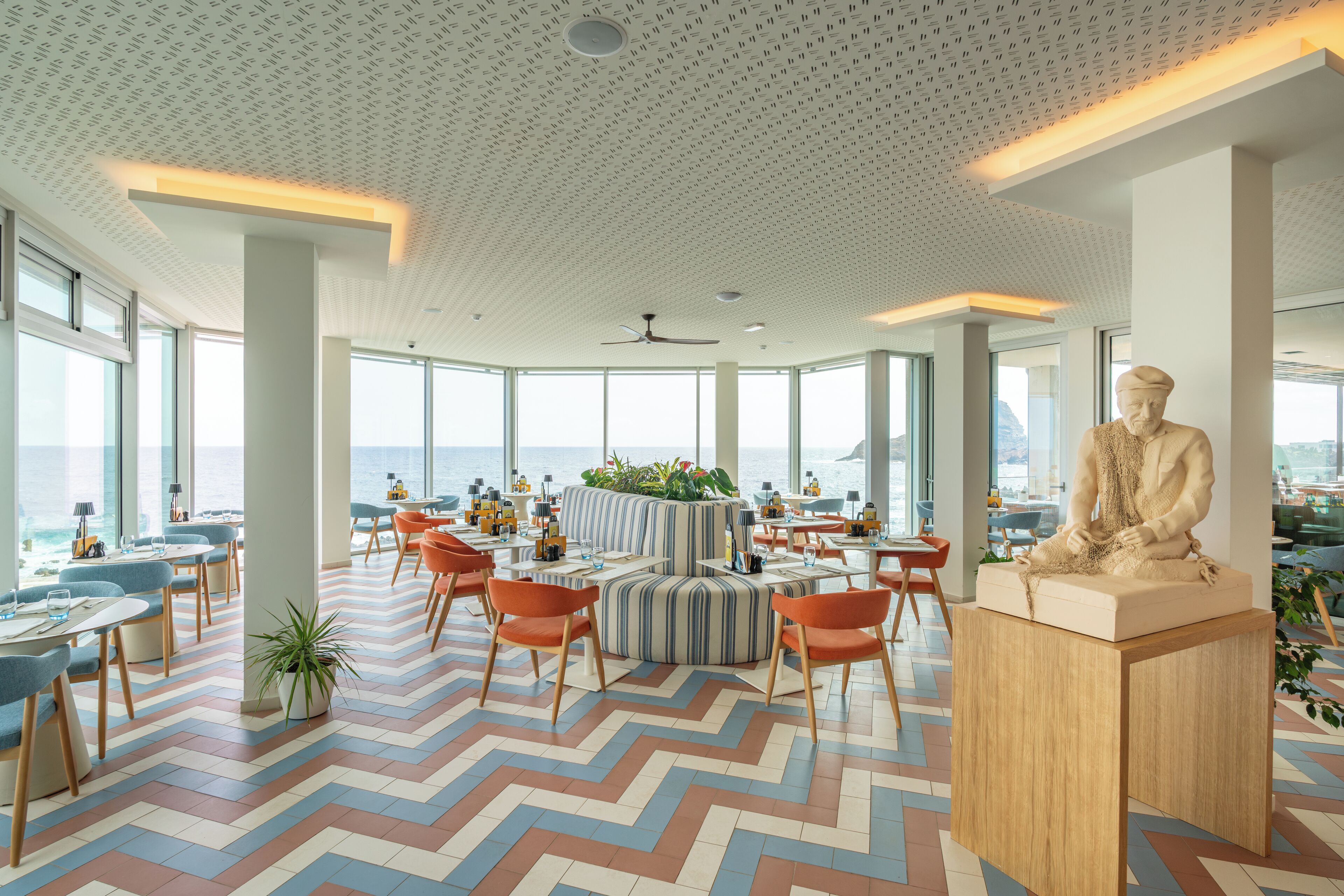 Un comedor moderno con amplios ventanales, un área de estar central y una estatua.