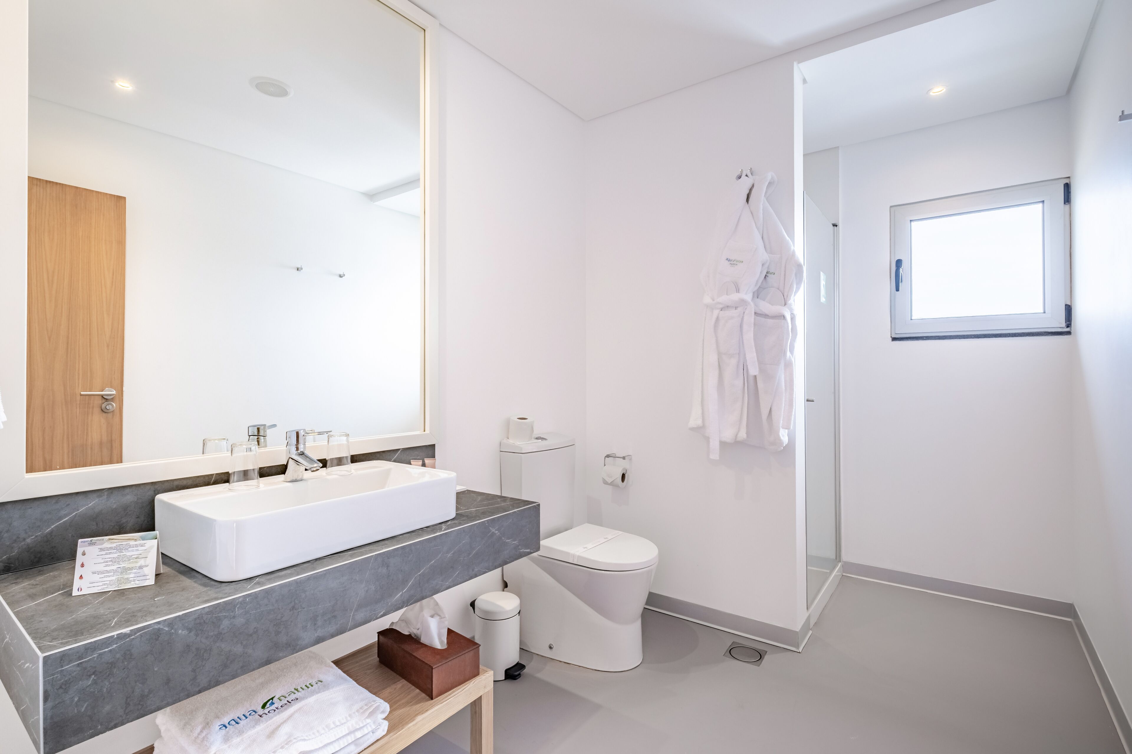 Une salle de bain moderne avec un grand miroir, des éléments d’équipement blancs, un plan de toilette en marbre, des toilettes et un espace douche.