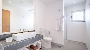 Un baño moderno con un espejo grande, sanitarios blancos, encimera de mármol, inodoro y zona de ducha.