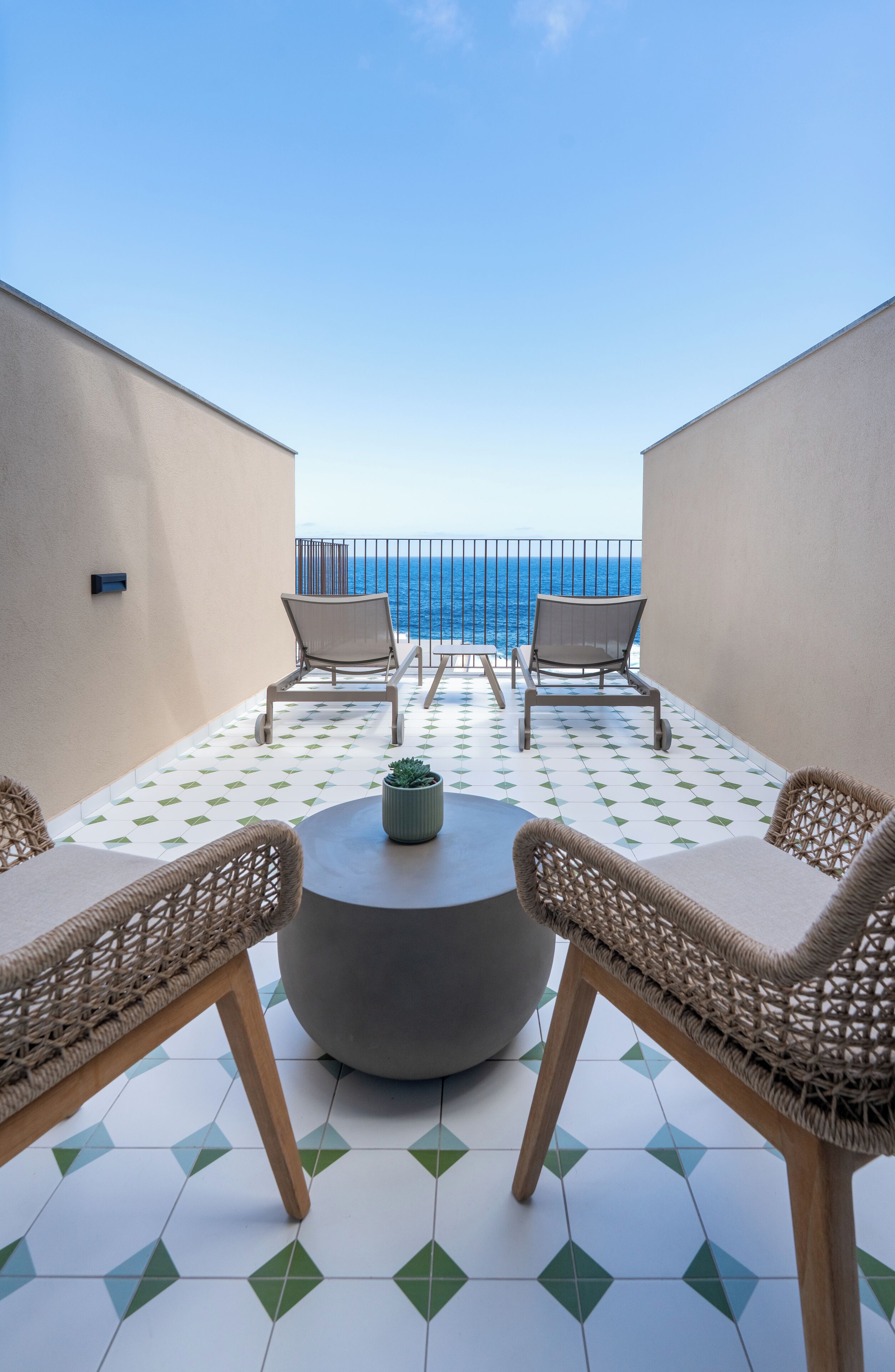 Una terraza con mobiliario de mimbre, una mesa redonda y una planta en maceta.