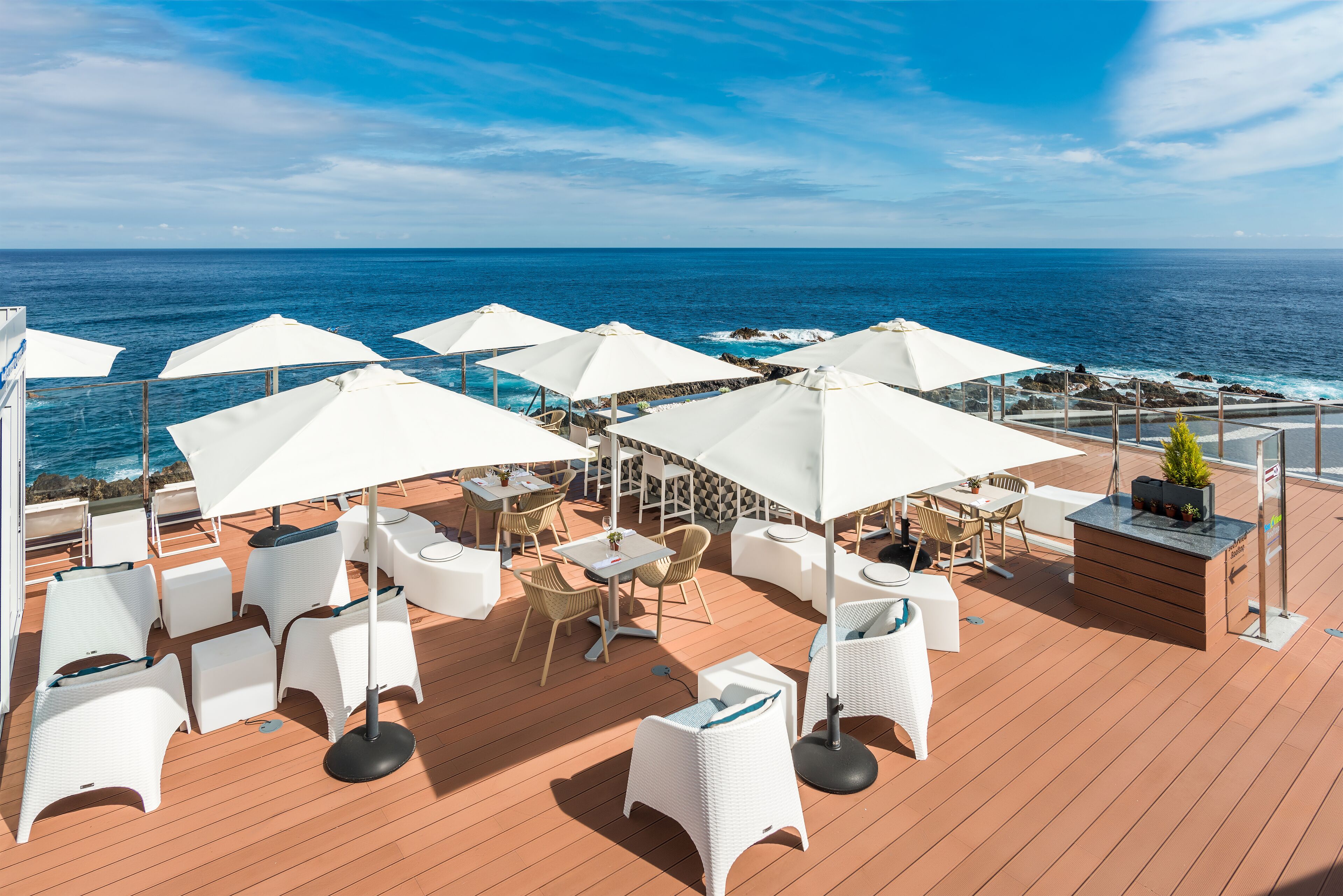 Een terras met witte rieten meubels en parasols, met uitzicht op de oceaan.