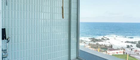 Un baño con vista al océano, un cabezal de ducha en forma de cubo de madera y paredes de azulejos.