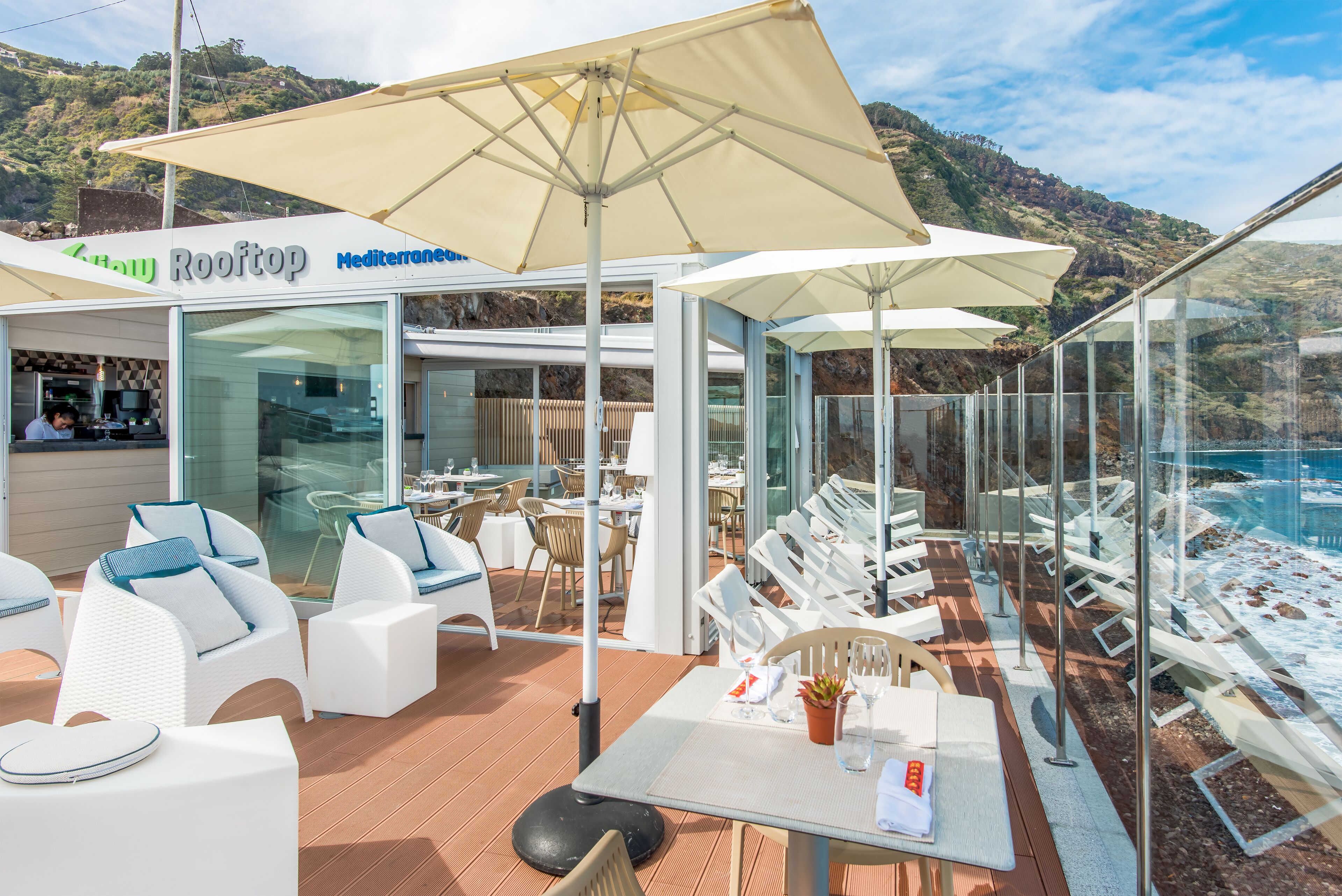 A rooftop restaurant with outdoor seating, a view of the sea, and a sign reading "Rooftop Mediterranean."