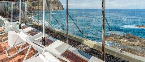 A deck with sun loungers and umbrellas overlooking a rocky coastline and the sea.