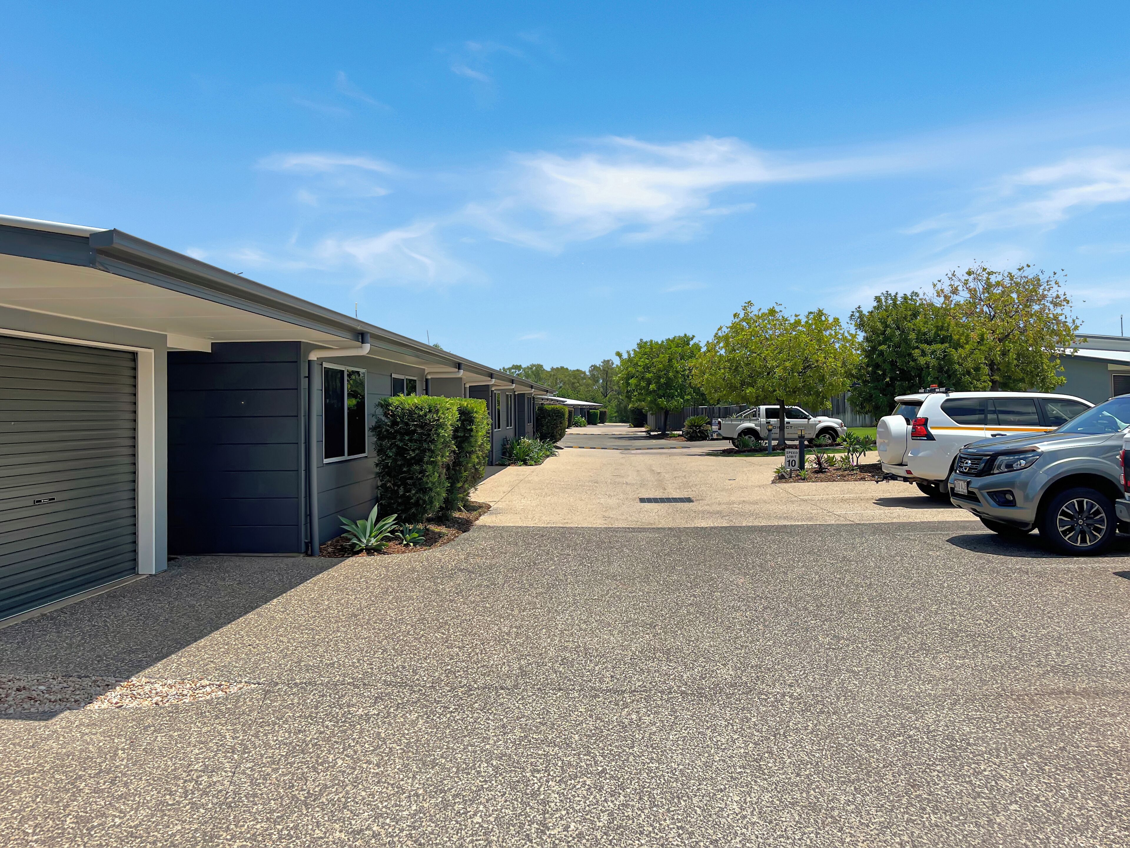 A row of modern, single-story buildings with a gravel driveway and parked vehicles.