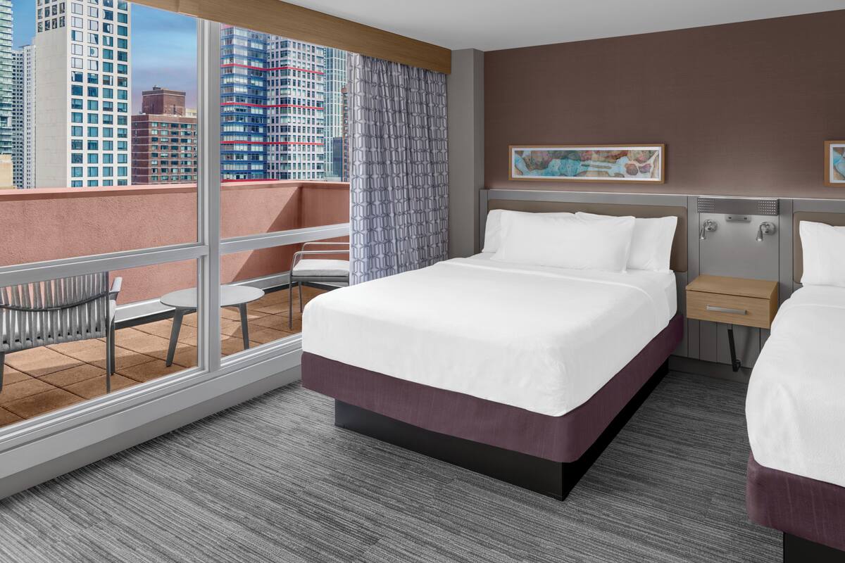 Ein Hotelzimmer mit einem großen Bett, einem kleinen Schreibtisch, einem Sessel und einem Balkon mit Stadtblick.