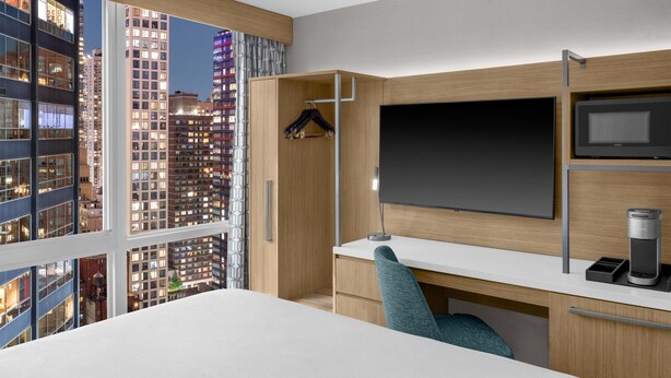 Een moderne hotelkamer met een groot bed, een bureau met een computer, een televisie en een koffiezetapparaat.