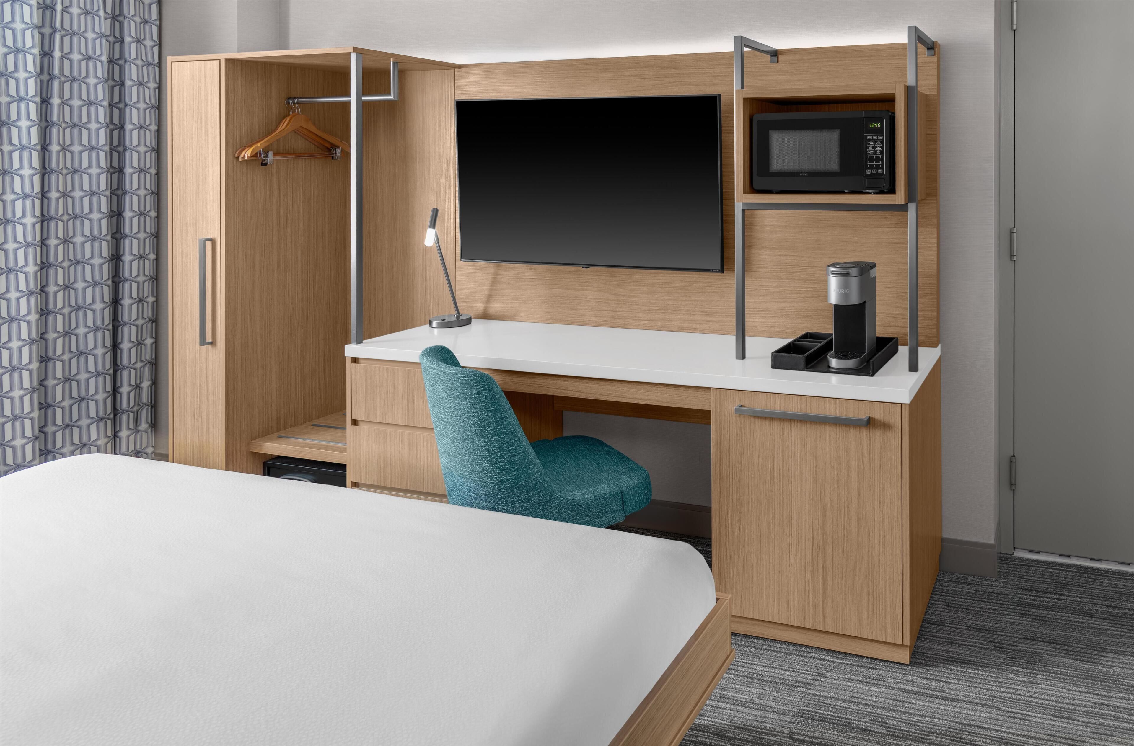 A hotel room with a bed, a desk with a chair, a TV, a microwave, and a coffee machine.