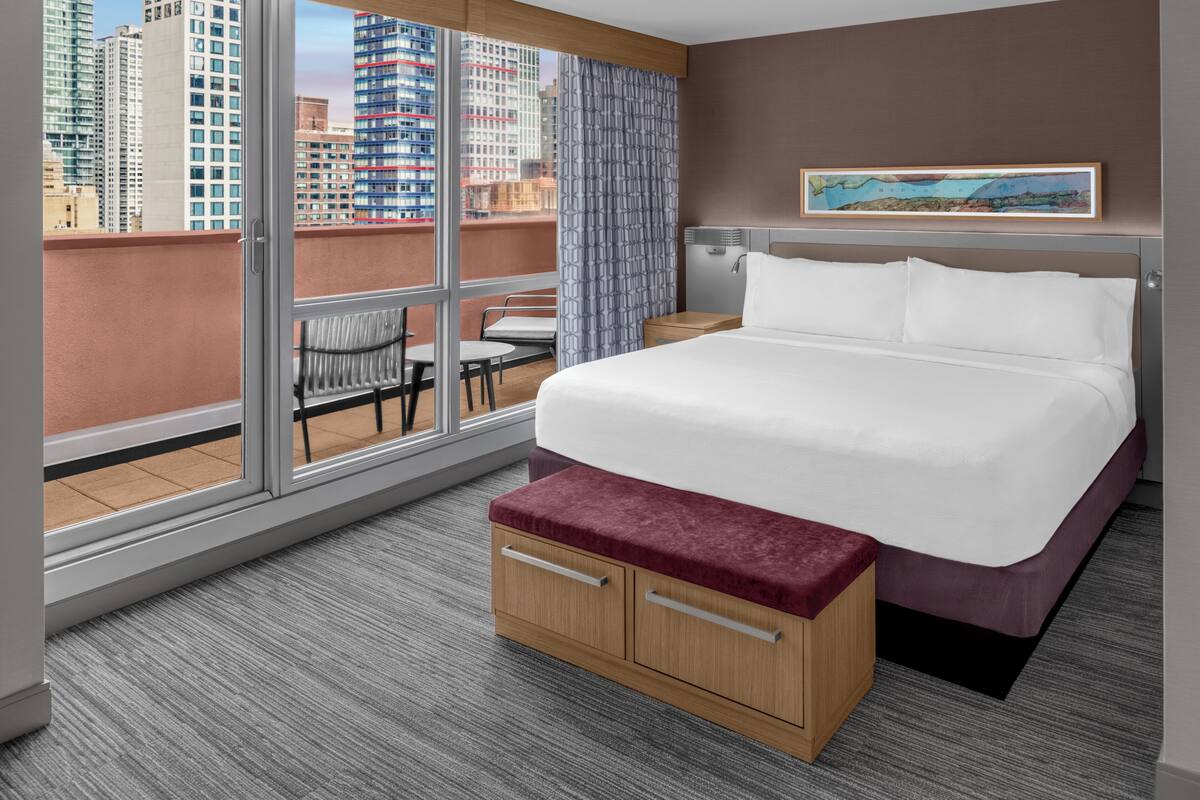 Ein Hotelzimmer mit einem großen Bett, einer Holzbank, einem kleinen Tisch und einem Stuhl.