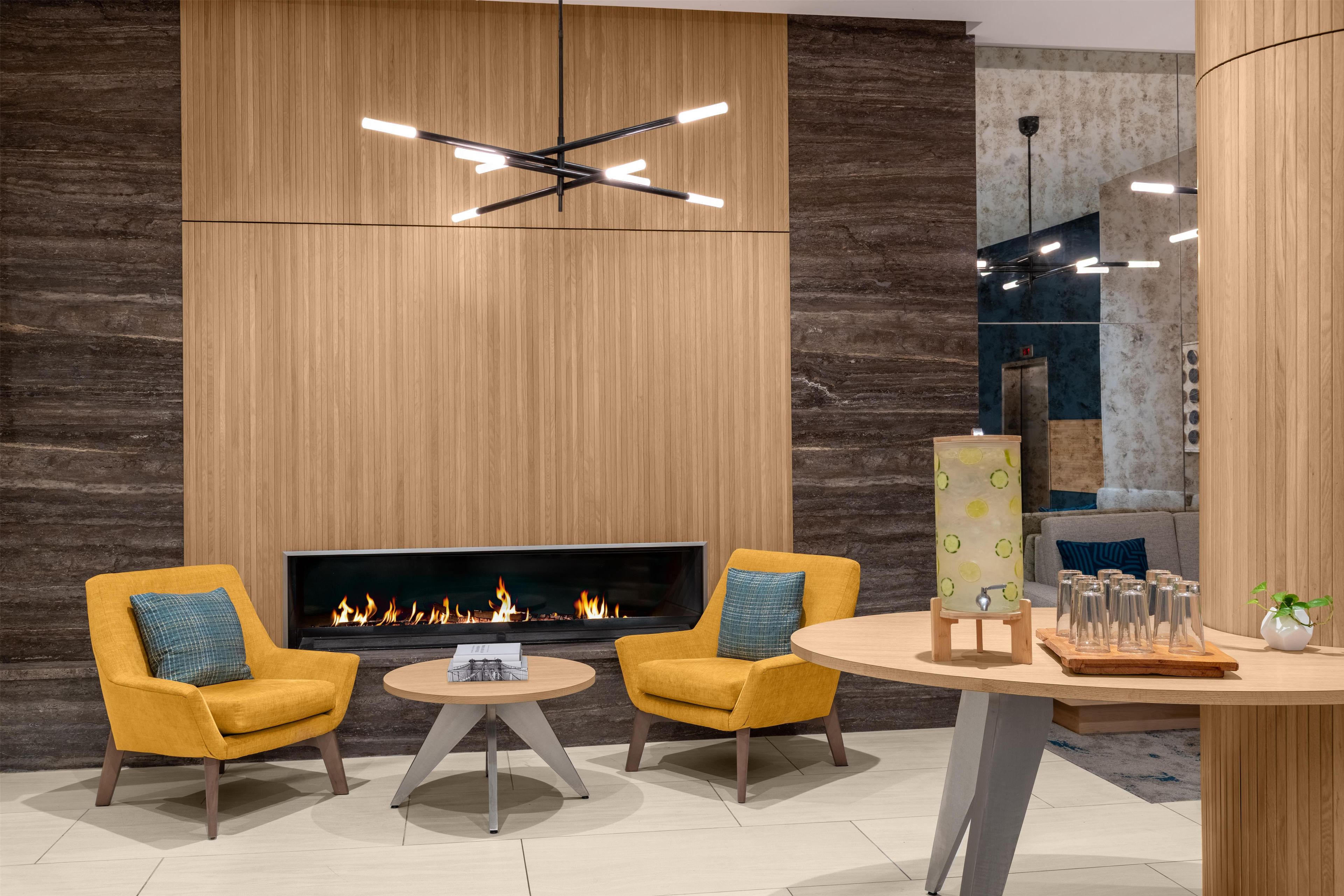A modern lounge area with a fireplace, two yellow armchairs, a round table, and a contemporary light fixture.