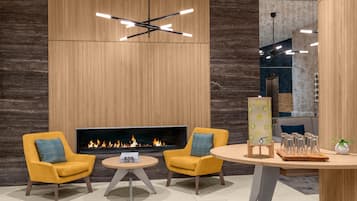 A modern lounge area with a fireplace, two yellow armchairs, a round table, and a contemporary light fixture.
