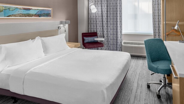 Une chambre d’hôtel avec un lit, un bureau, une chaise, une carte accrochée au mur et une fenêtre avec des rideaux.