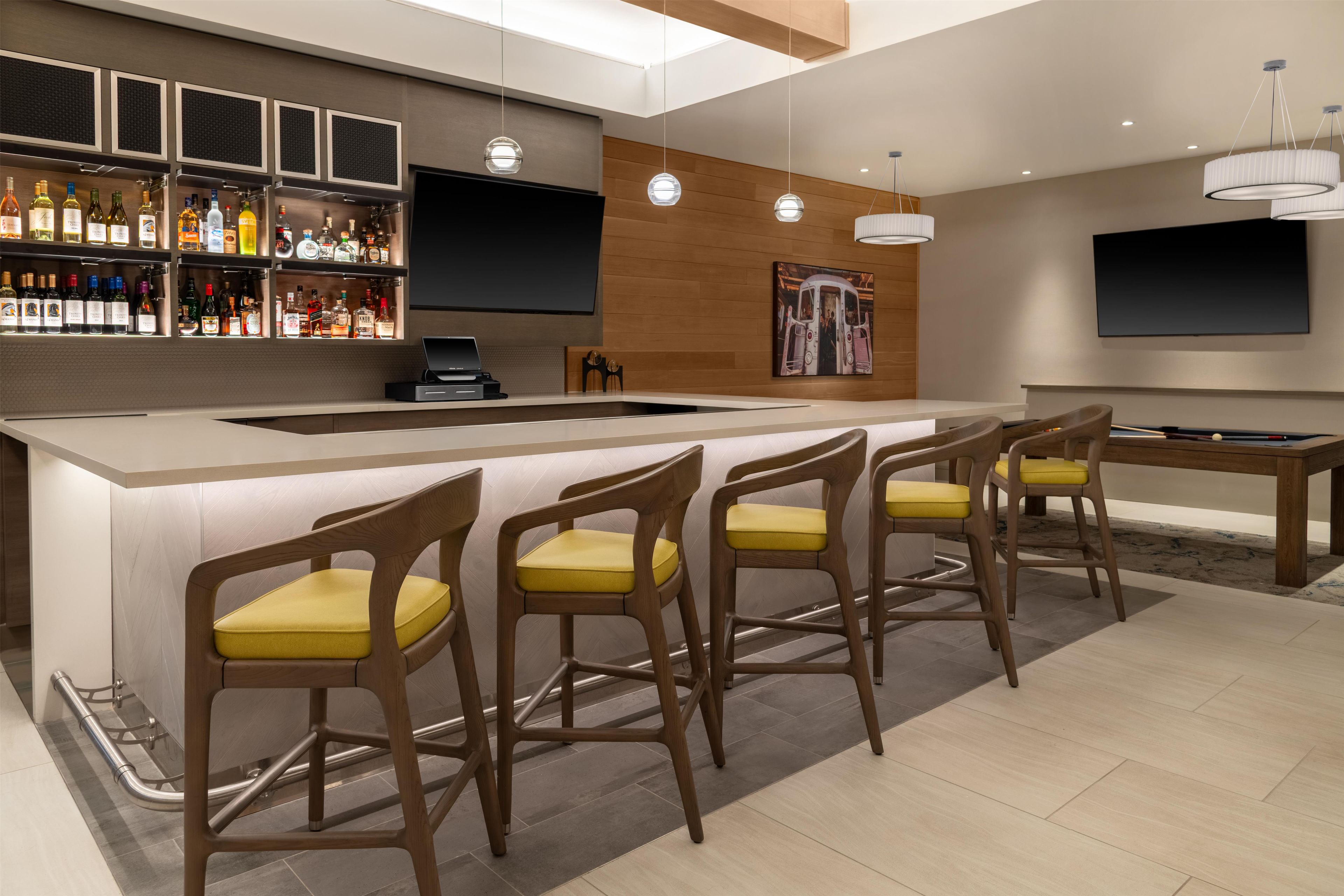 Eine moderne Bar mit einer langen Theke, zahlreichen Flaschen Spirituosen und einem Flachbildfernseher.