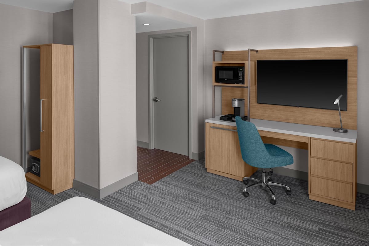 Ein Hotelzimmer mit einem Bett, einem Schreibtisch mit Stuhl, einer Mikrowelle, einem Flachbildfernseher und einem Kleiderschrank.