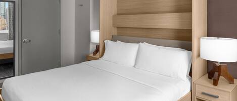 Una habitación de hotel con una cama grande, un cabecero de madera, una mesita de noche con una lámpara y una puerta que da a un baño.