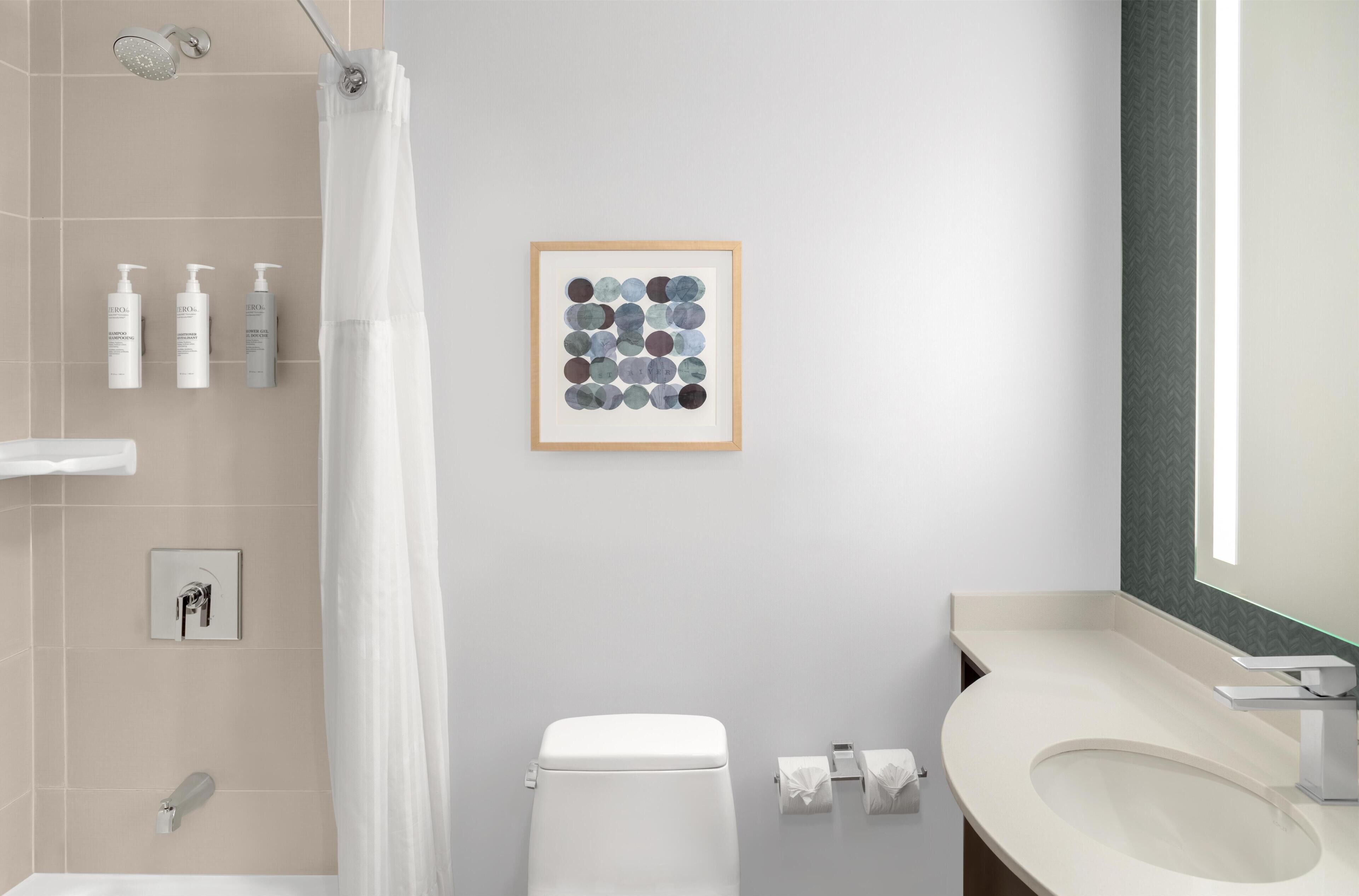 Een moderne badkamer met toilet, wastafel, douche en een kunstwerk in een lijst aan de muur.