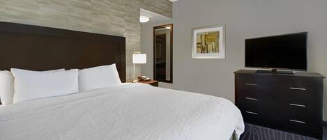 A hotel room with a large bed, a flat-screen TV, a dresser, a nightstand, a lamp, and a framed picture on the wall.
