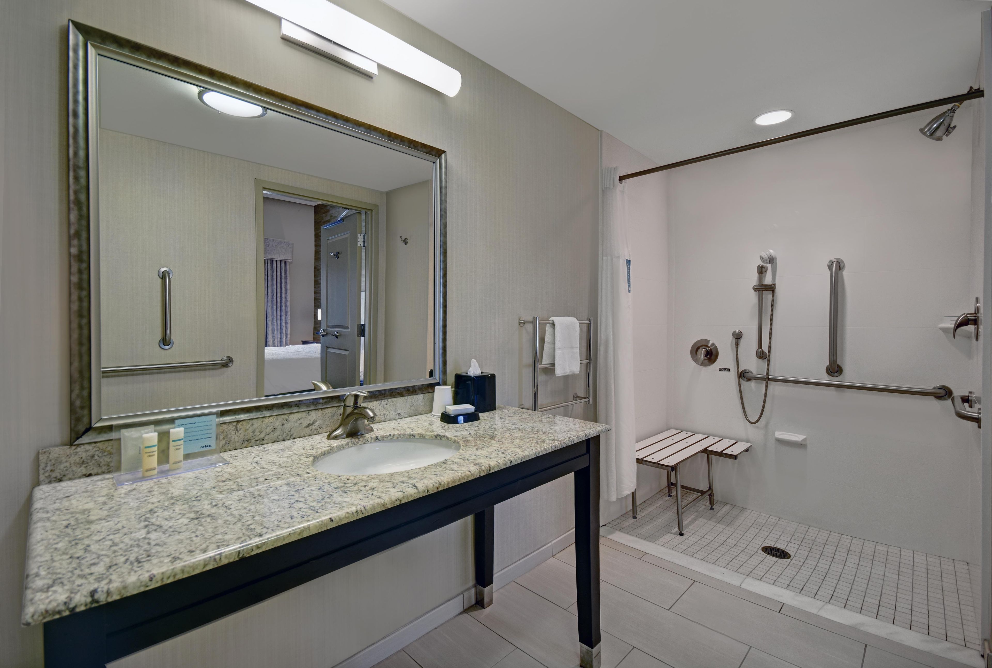 A modern bathroom with a large mirror, sink, and shower area.