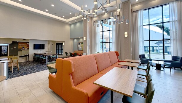 A modern hotel lobby with a large orange sofa, dining tables, and a TV screen.