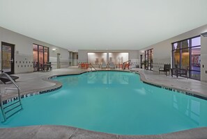 A swimming pool with a tiled edge, surrounded by chairs and tables, with doors leading to other areas.