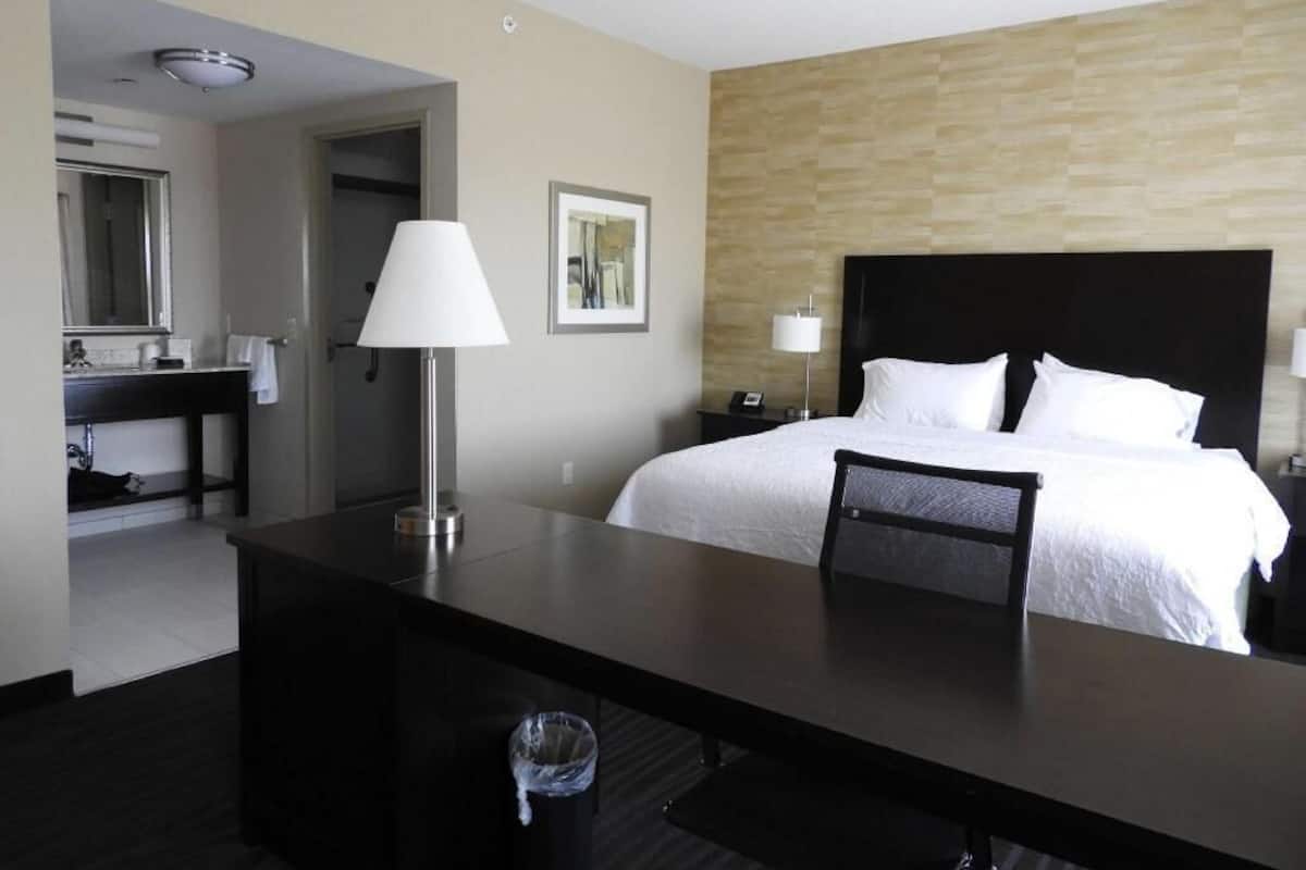 A hotel room with a bed, bedside table, lamp, and a desk with a chair.