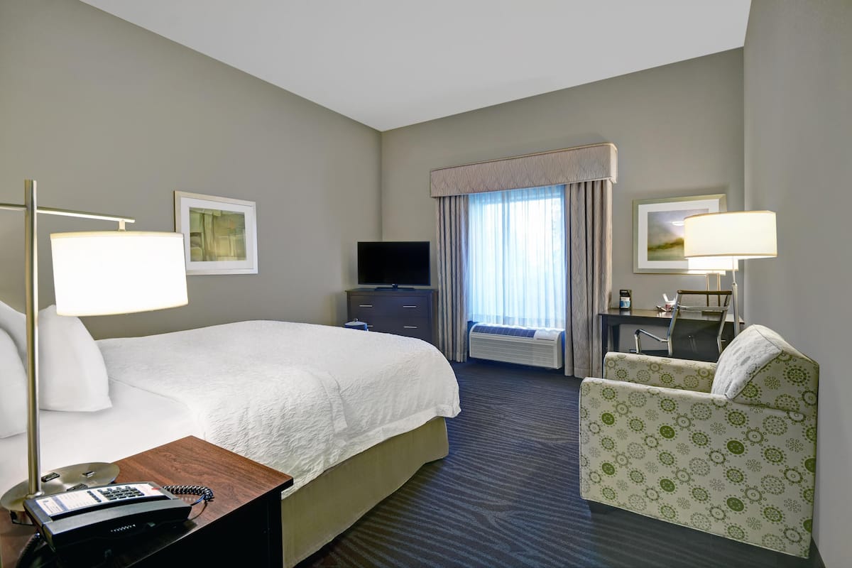 A hotel room with a bed, a desk with a telephone, a television, a chair, and a window with curtains.