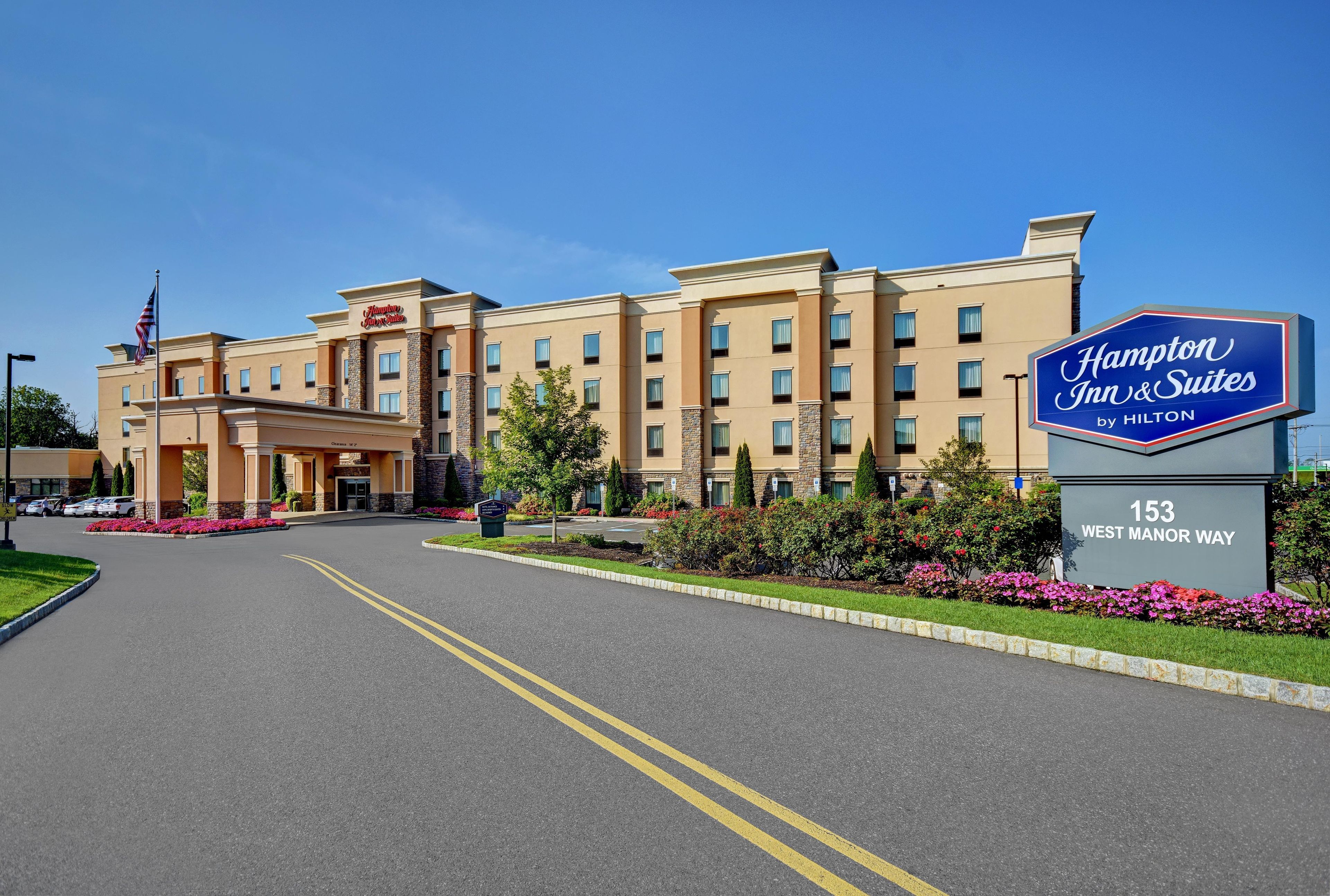 A Hampton Inn & Suites by Hilton hotel with a clear entrance, parking area, and a sign indicating the address.