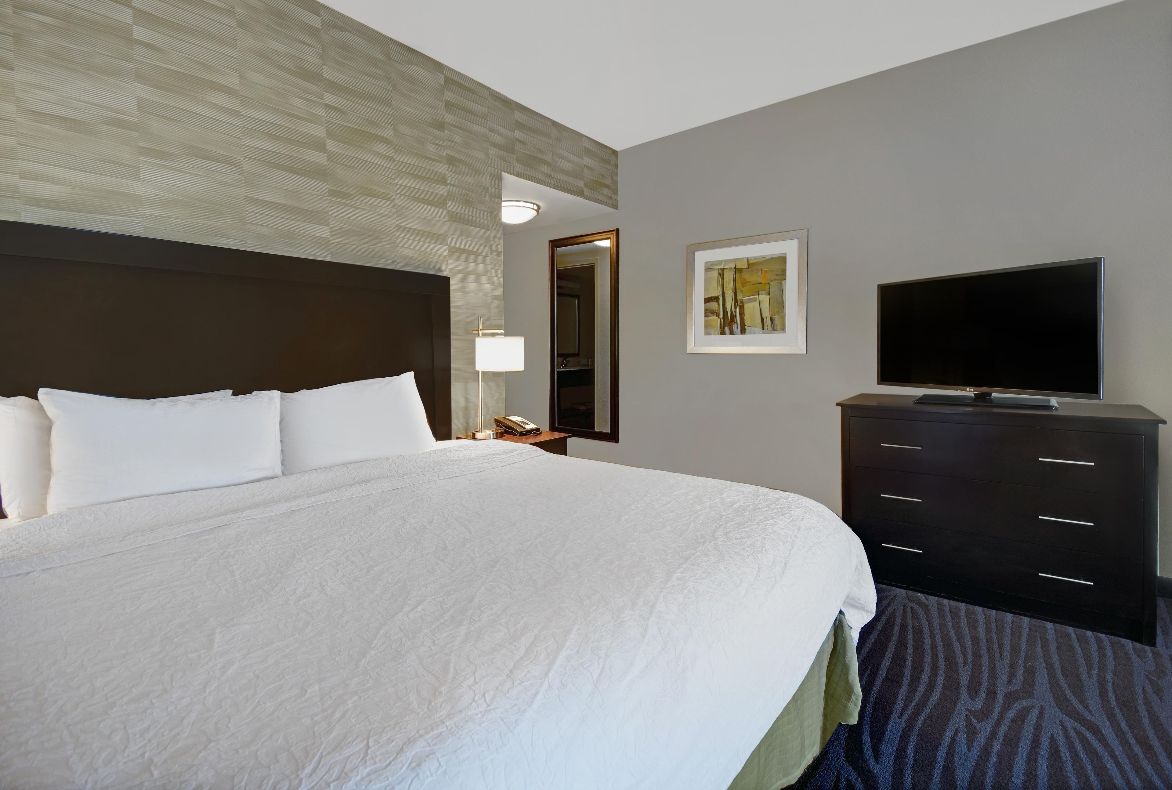 Una habitación de hotel con una cama grande, un televisor de pantalla plana, un aparador y un espejo.