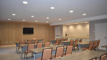 A conference room with tables and chairs, a flat-screen TV, and a kitchenette area.