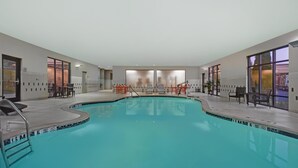 A swimming pool with a tiled edge, a lounge area with chairs, and a view of the outside.