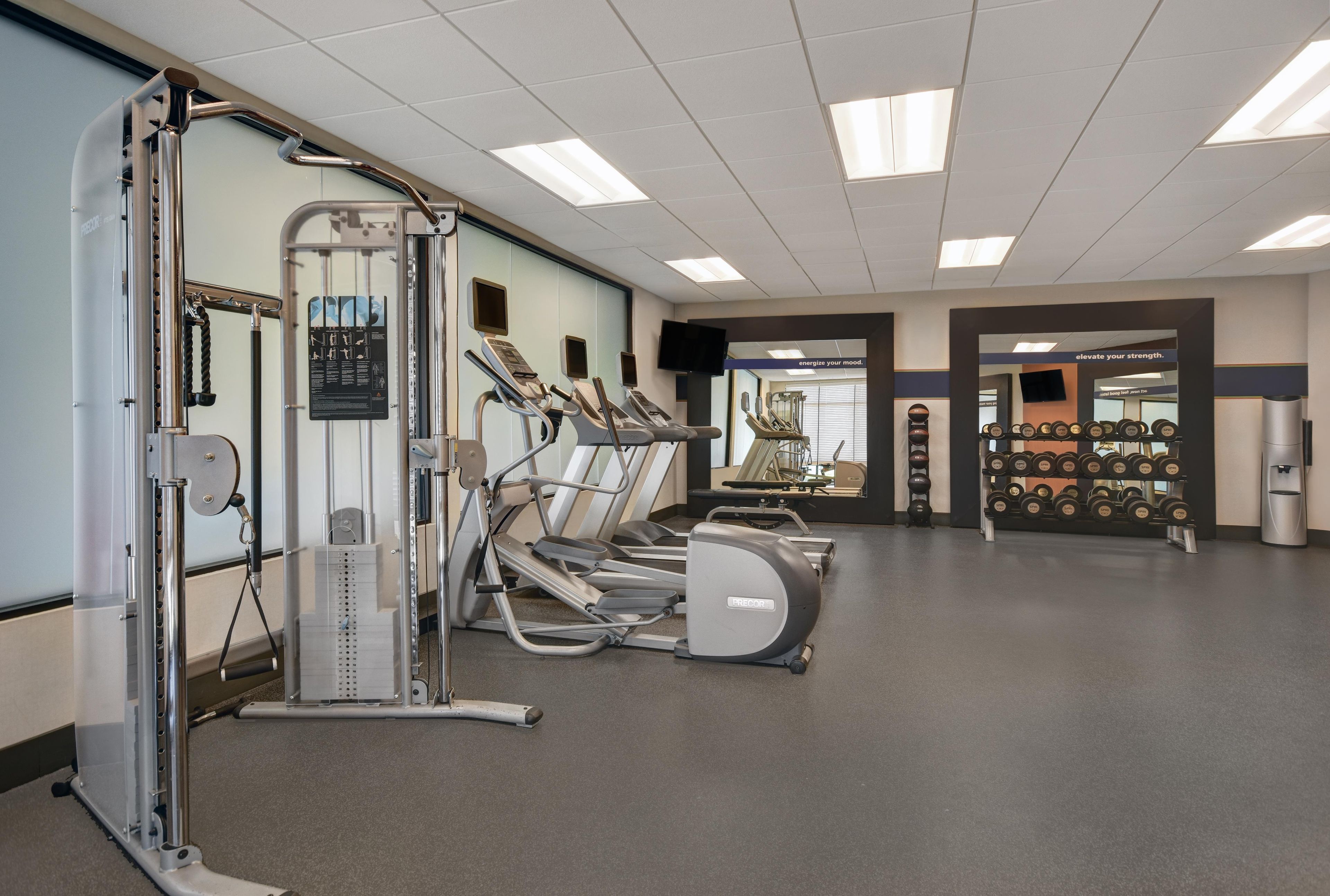 Ein Fitnessstudio mit Laufbändern, Kraftgeräten und einem an der Wand befestigten Fernseher.