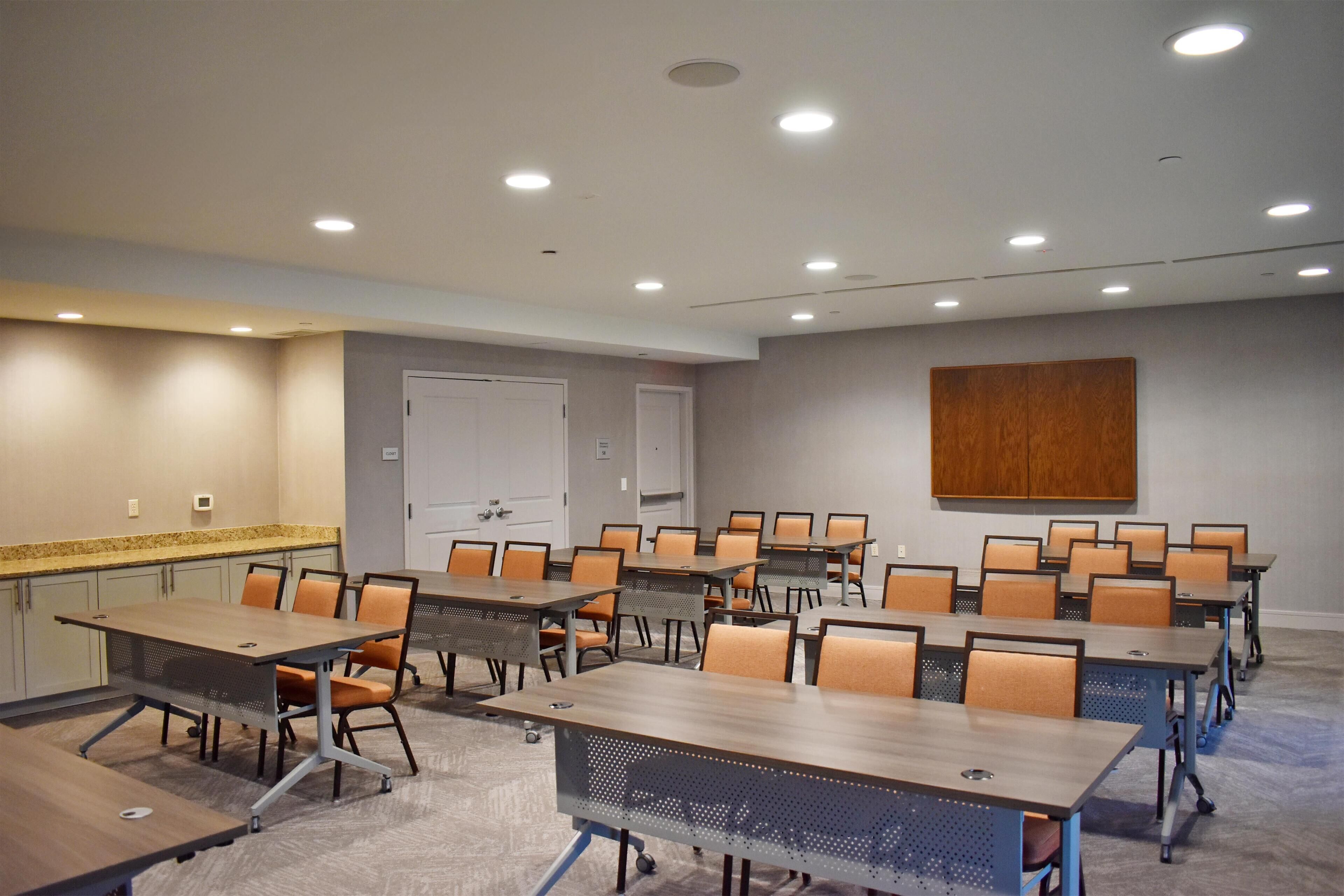 Un salón de conferencias con varias mesas y sillas, una pared de acento de madera y luces empotradas en el techo.