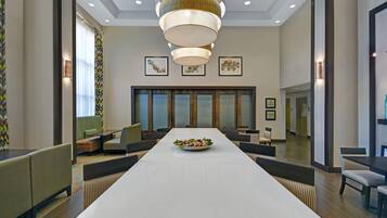Un salón de conferencias con una larga mesa, sillas, una lámpara decorativa y cuadros en las paredes.