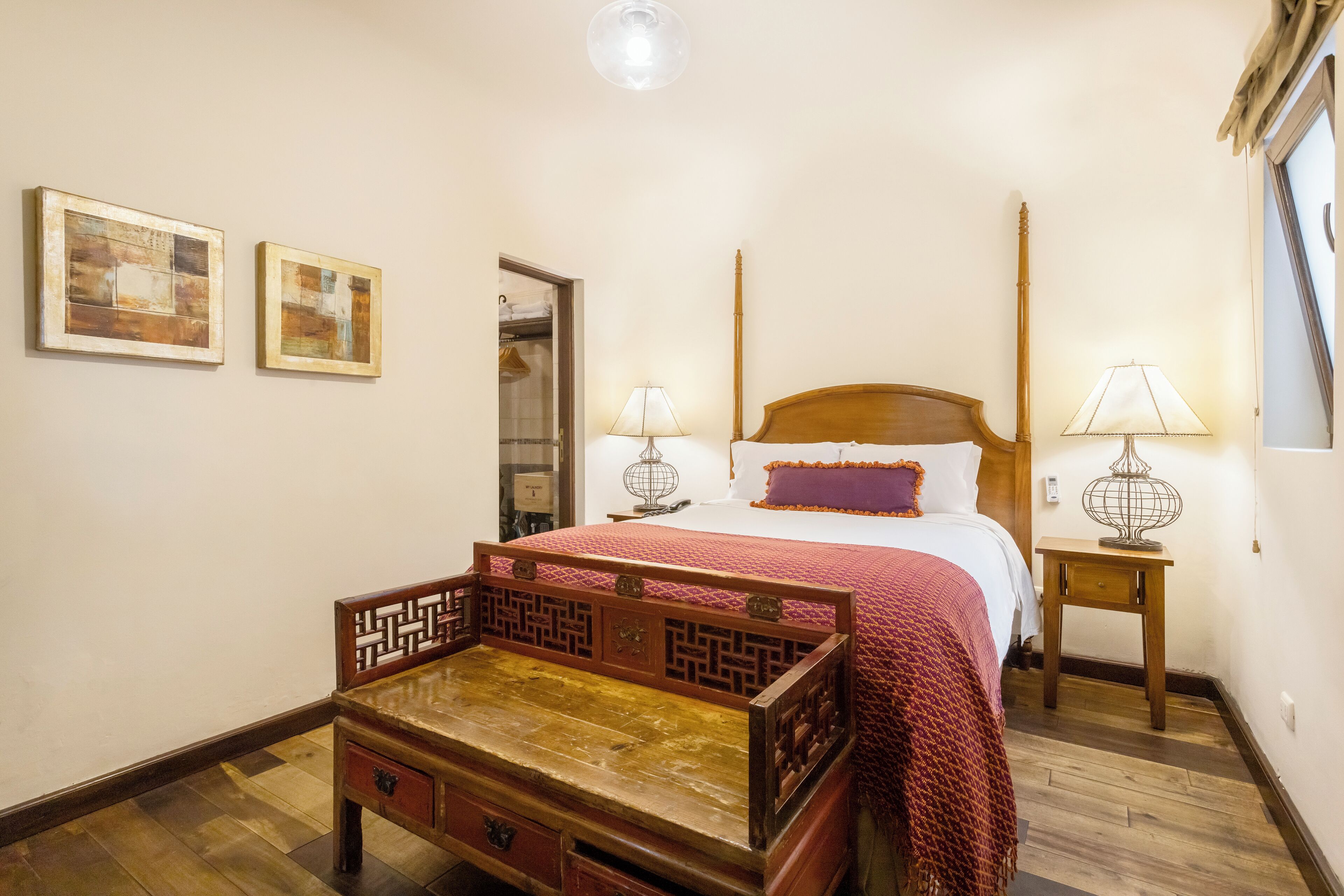 A traditional wooden bed with a red bedspread, two bedside lamps, and a small wooden nightstand.