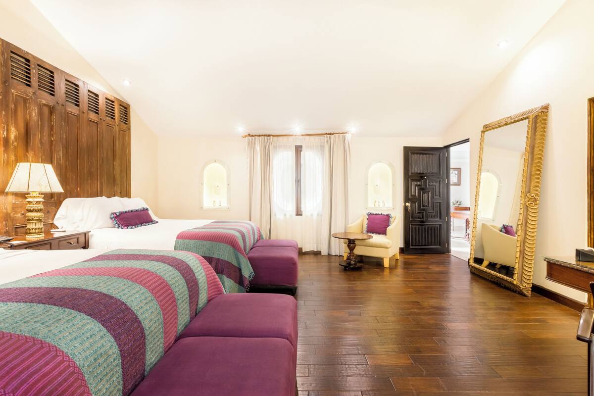 A hotel room with a large bed, two sofas, a small table, and a mirror.