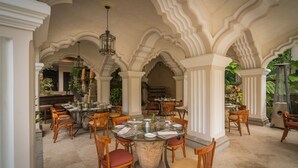 Un amplio espacio exterior para comer con varias mesas y sillas redondas, rodeado de columnas y arcos blancos.