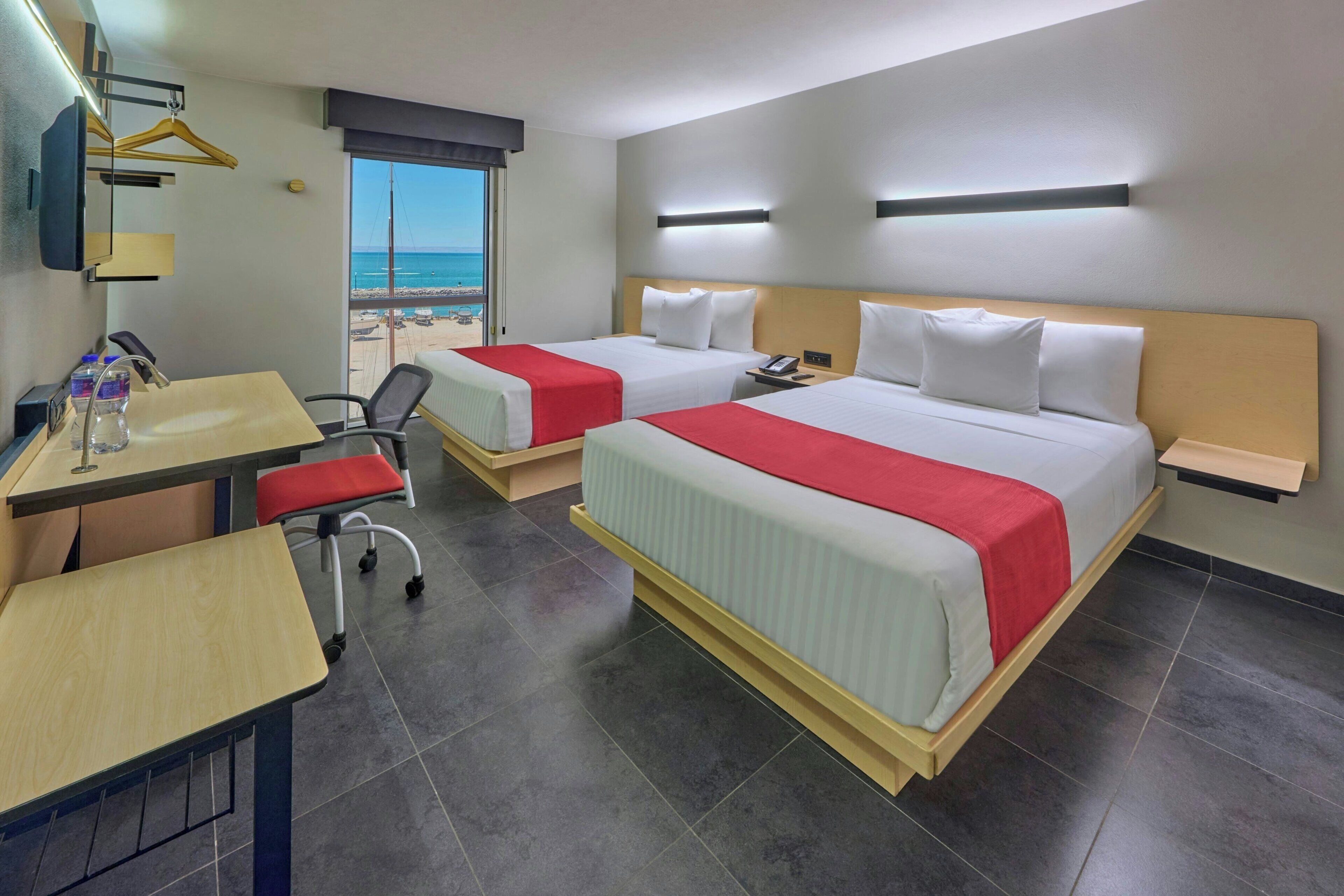 Ein Hotelzimmer mit zwei Betten, einem Schreibtisch, einem Sessel und Meerblick.