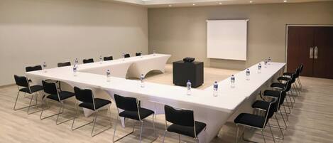 Un salón de conferencias con una larga mesa, sillas, un proyector y una pizarra.